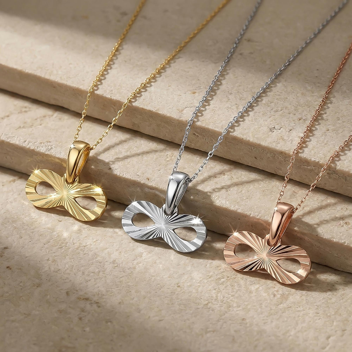 14K yellow, white and rose gold infinity necklaces on a stone ledge