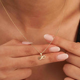 Fingers holding a 14K yellow gold diamond-cut infinity pendant on the neck