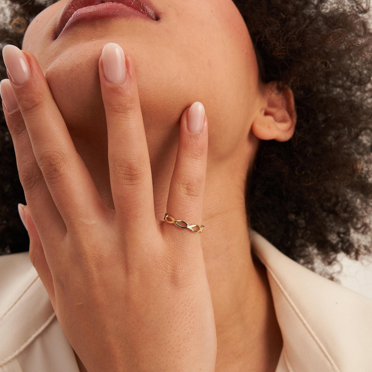 Bague infini ajourée en or jaune 14 carats sur une main au menton du mannequin