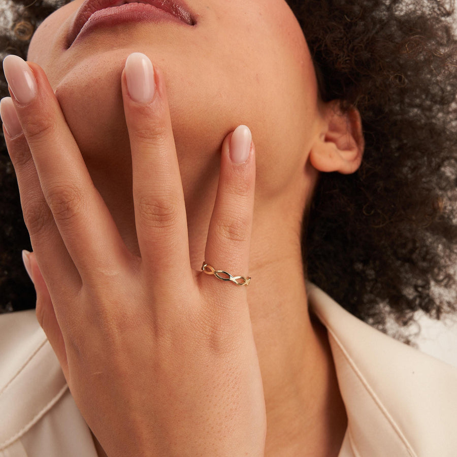 Bague infini ajourée en or jaune 14 carats sur une main au menton du mannequin
