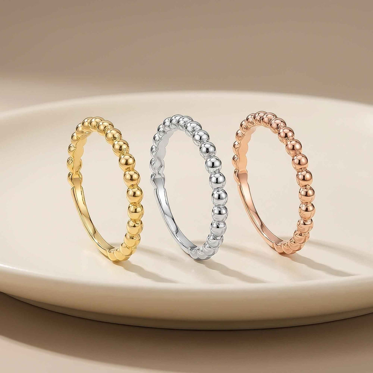 Anillos burbuja en oro amarillo, blanco y rosa de 14 quilates en vertical sobre un plato blanco