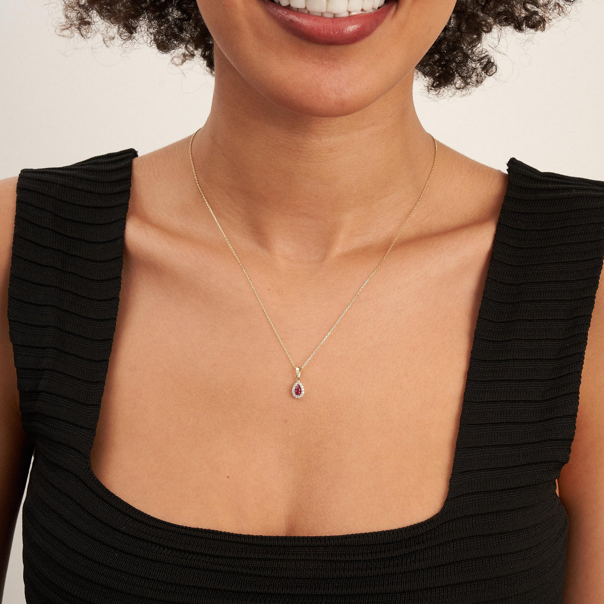 Model in schwarzem Oberteil mit tropfenförmiger Halo-Halskette mit laborgezüchtetem Rubin aus 585er Gelbgold