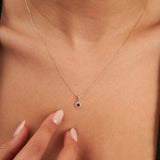 Gros plan du collier halo rubis rond de synthèse en or jaune 14 carats, bout des doigts au niveau du décolleté