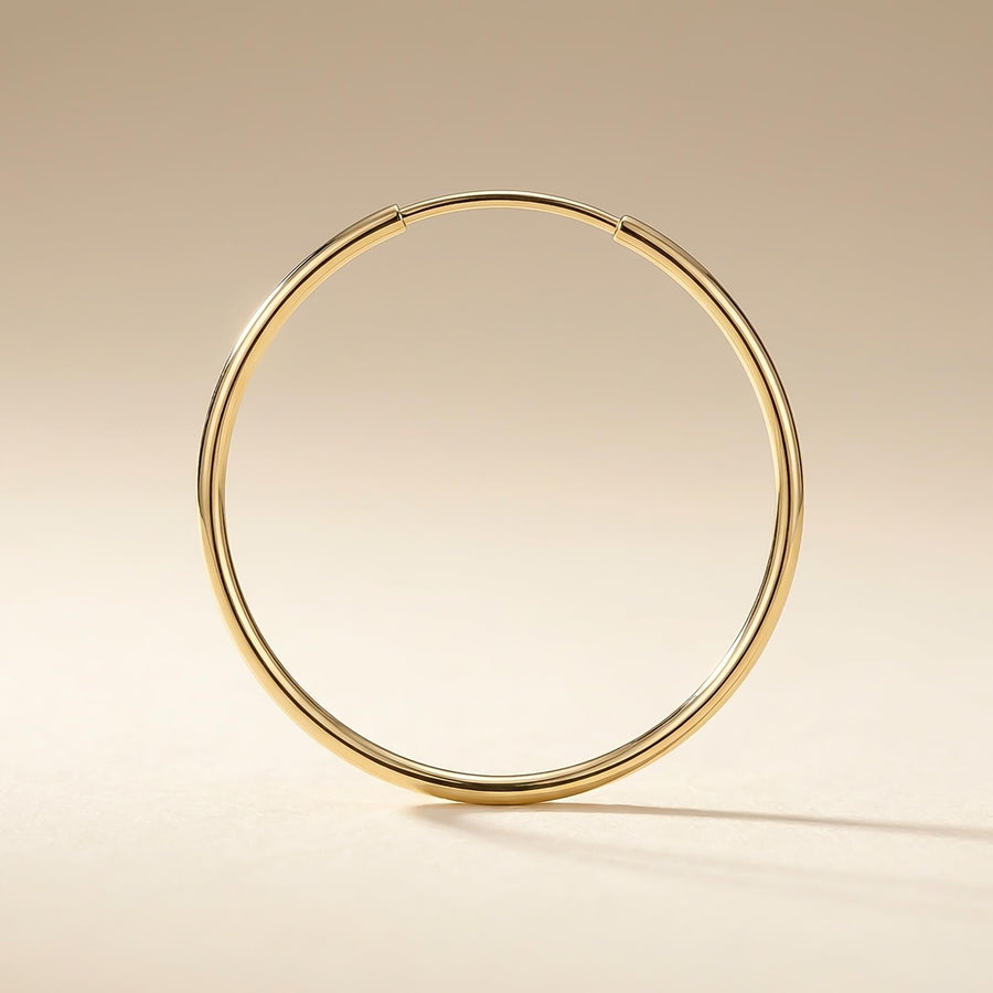 Singolo orecchino a cerchio endless in oro giallo 14kt posato in verticale su una superficie beige