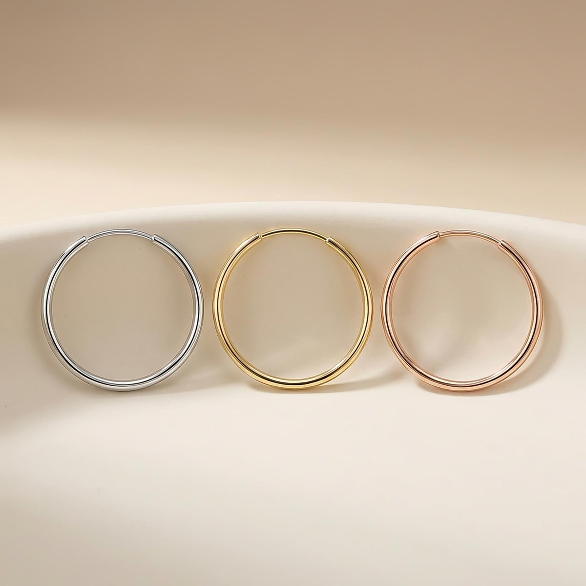 Orecchini a cerchio endless in oro bianco, giallo e rosa 14kt su un piattino di ceramica