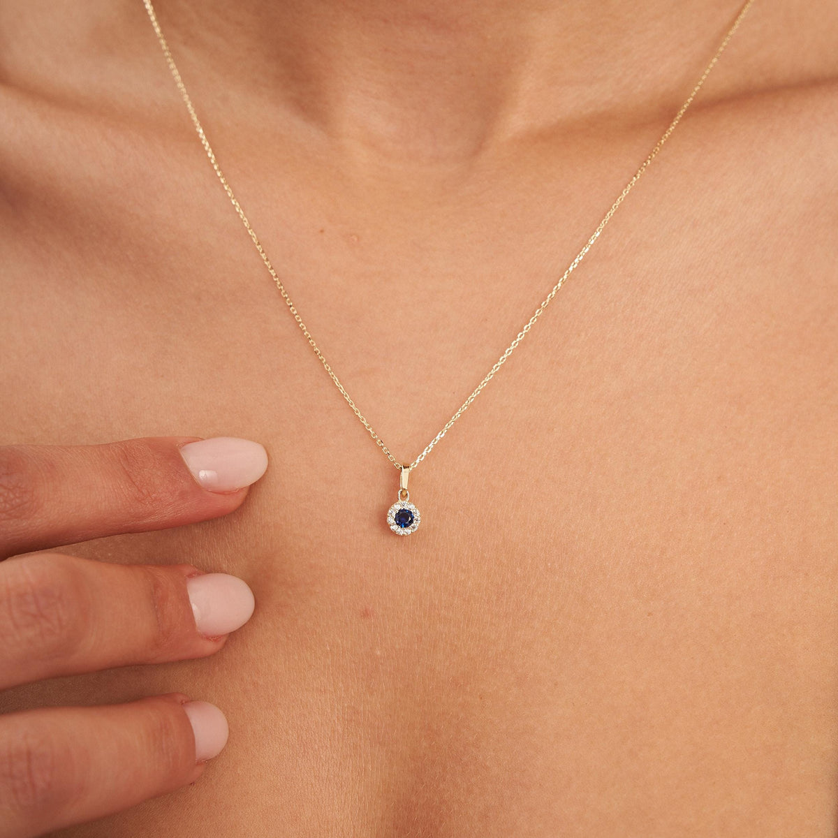 Gros plan du pendentif halo saphir rond de synthèse en or jaune 14 carats, bout des doigts en dessous