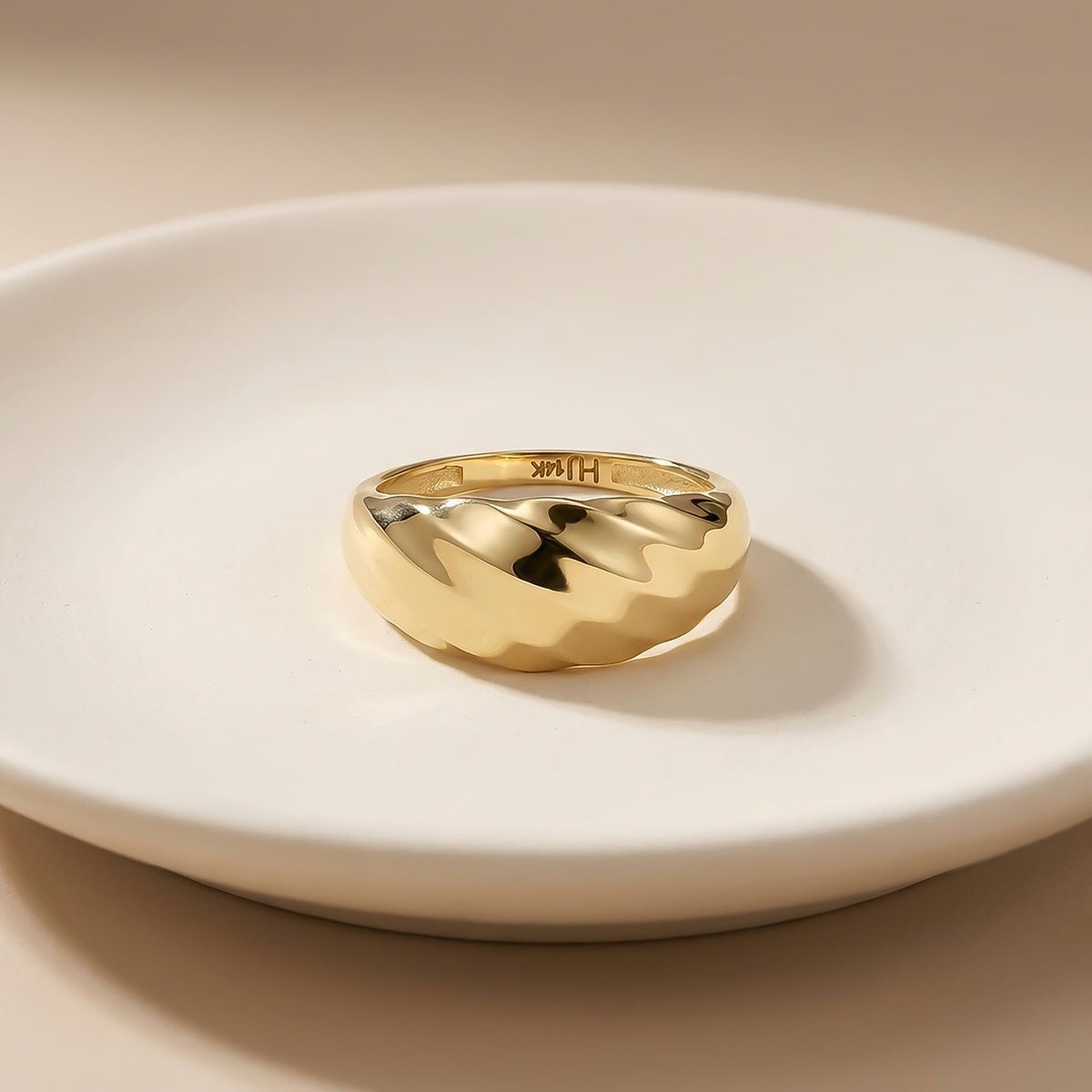Kuppelring mit Wirbelmuster aus 585er Gelbgold auf weißem Teller, Gravur an der Innenseite sichtbar