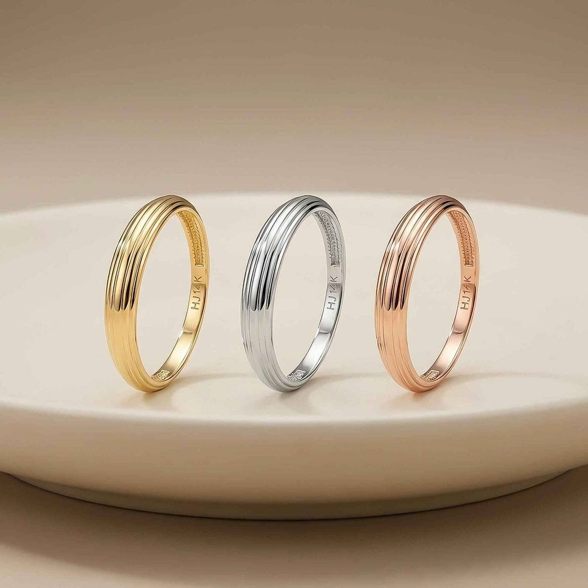 Anillos acanalados en oro amarillo, blanco y rosa de 14 quilates en vertical sobre un plato blanco