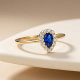 14K yellow gold pear halo ring with lab-grown sapphire on beige backdrop