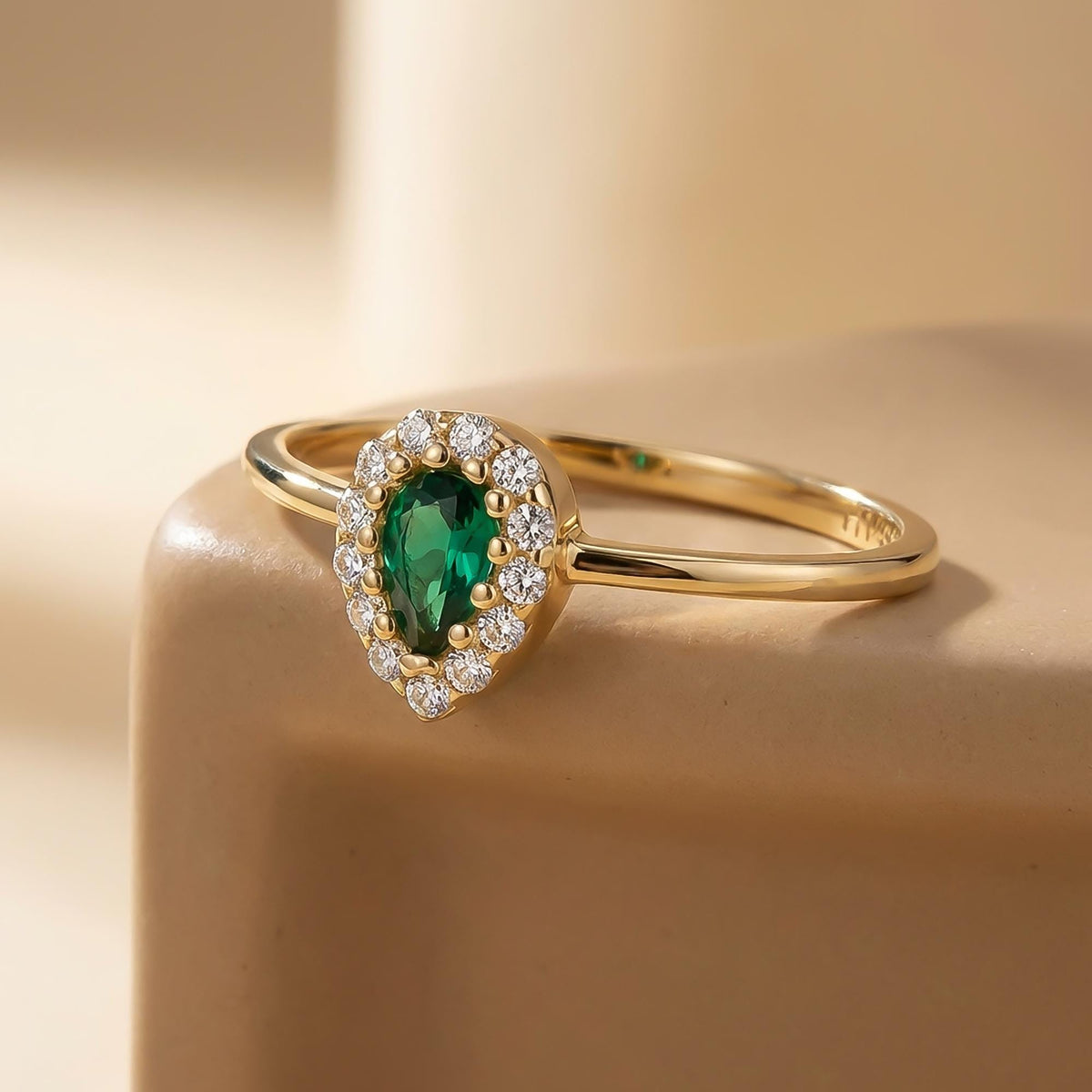 14K yellow gold pear halo ring with lab-grown emerald on a beige pedestal