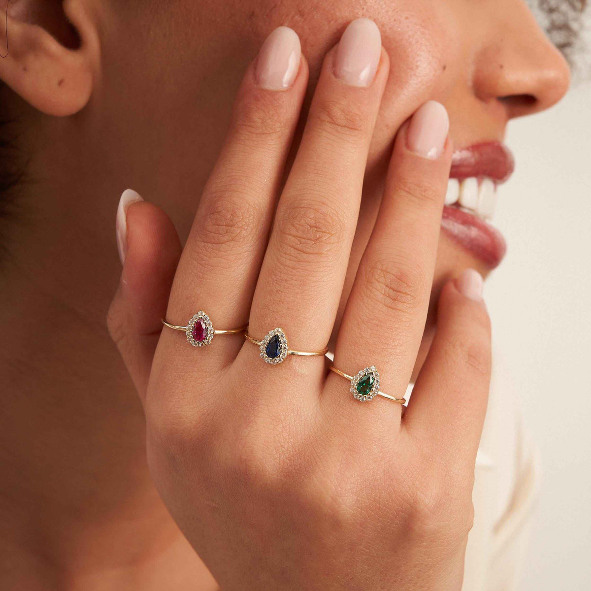 Model wearing 14K yellow gold pear halo rings with lab-grown ruby and emerald