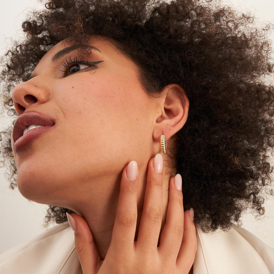 Model mit Blick nach oben und Hand am Hals trägt gerippte Croissant-Creolen aus 585er Gelbgold