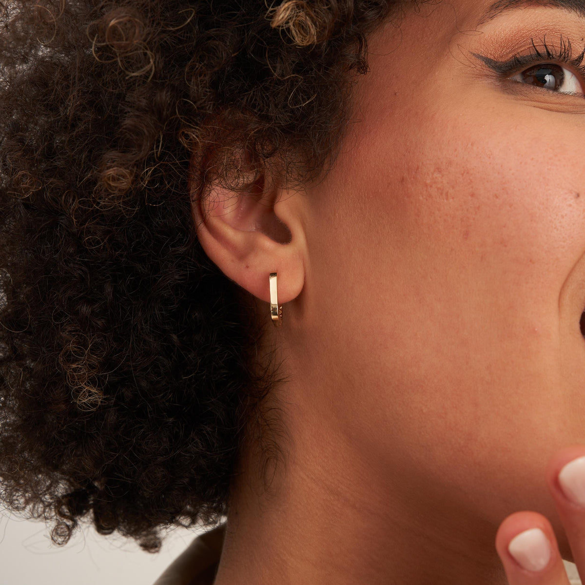 Close-up of a 14K yellow gold square hoop earring on the lobe, the model looking on