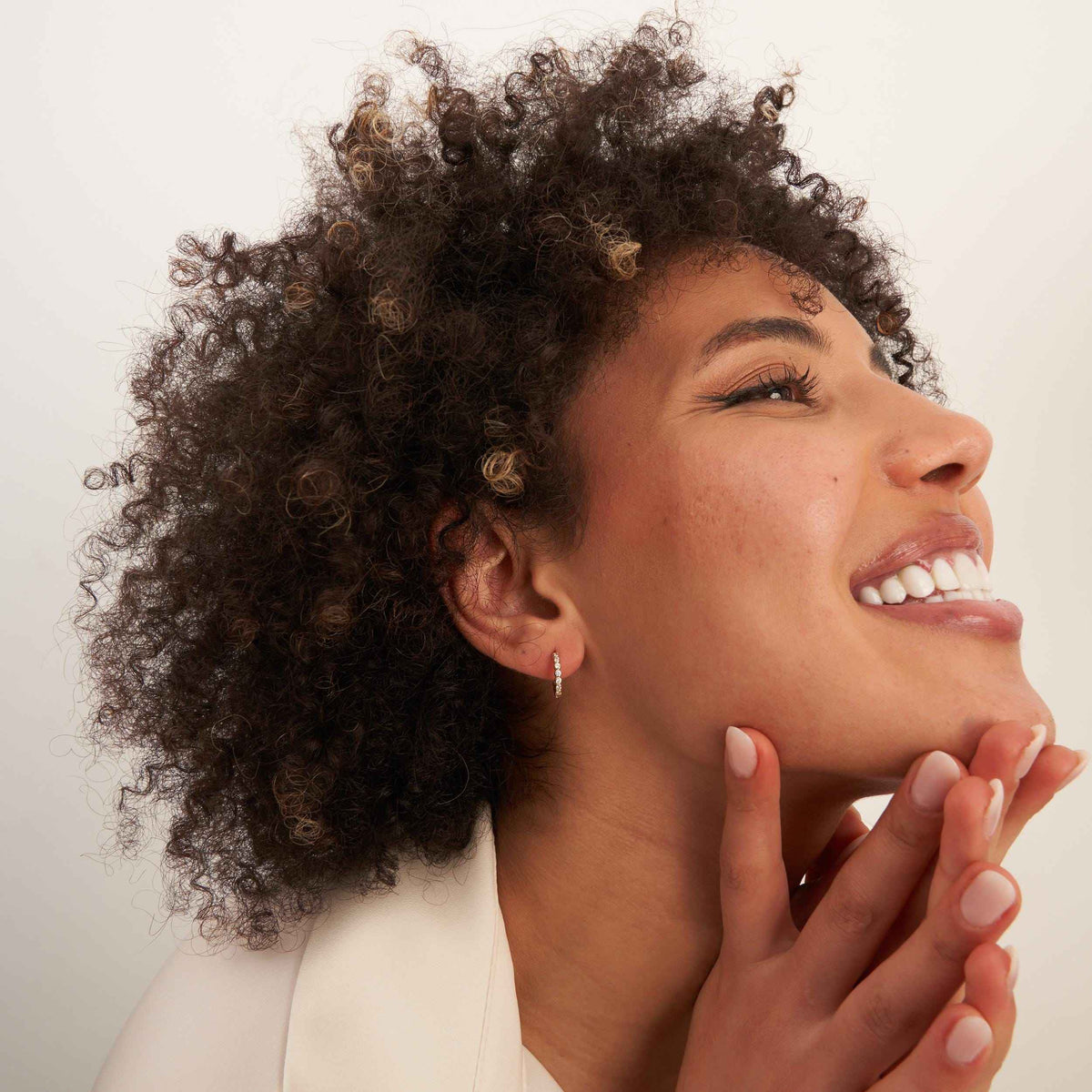 Créoles à oxydes de zirconium en serti clos en or jaune 14 carats portées par un mannequin souriant, la tête inclinée en arrière et les doigts au menton