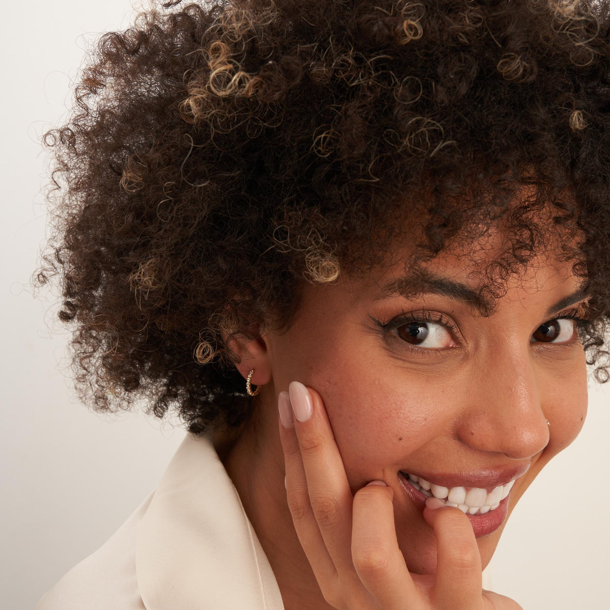 Créoles à oxydes de zirconium en serti clos en or jaune 14 carats portées par un mannequin souriant, la main sur la joue