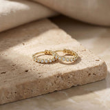 Paire de créoles à oxydes de zirconium en serti clos en or jaune 14 carats sur un bloc de travertin