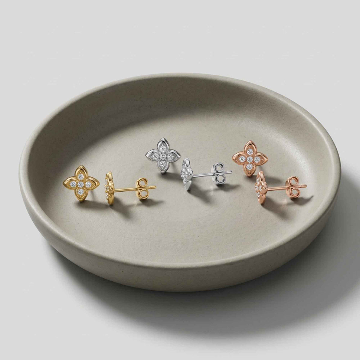 Puces d'oreilles fleur en oxyde de zirconium et or jaune, blanc et rose 14 carats sur une coupelle en céramique grise