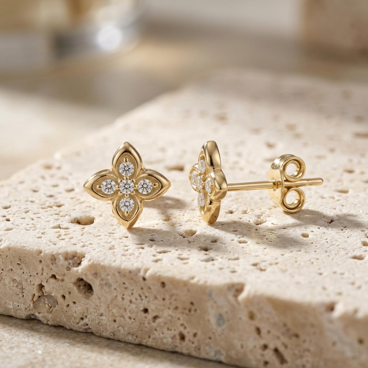 Puces d'oreilles fleur à quatre feuilles en oxyde de zirconium et or jaune 14 carats sur une pierre en travertin