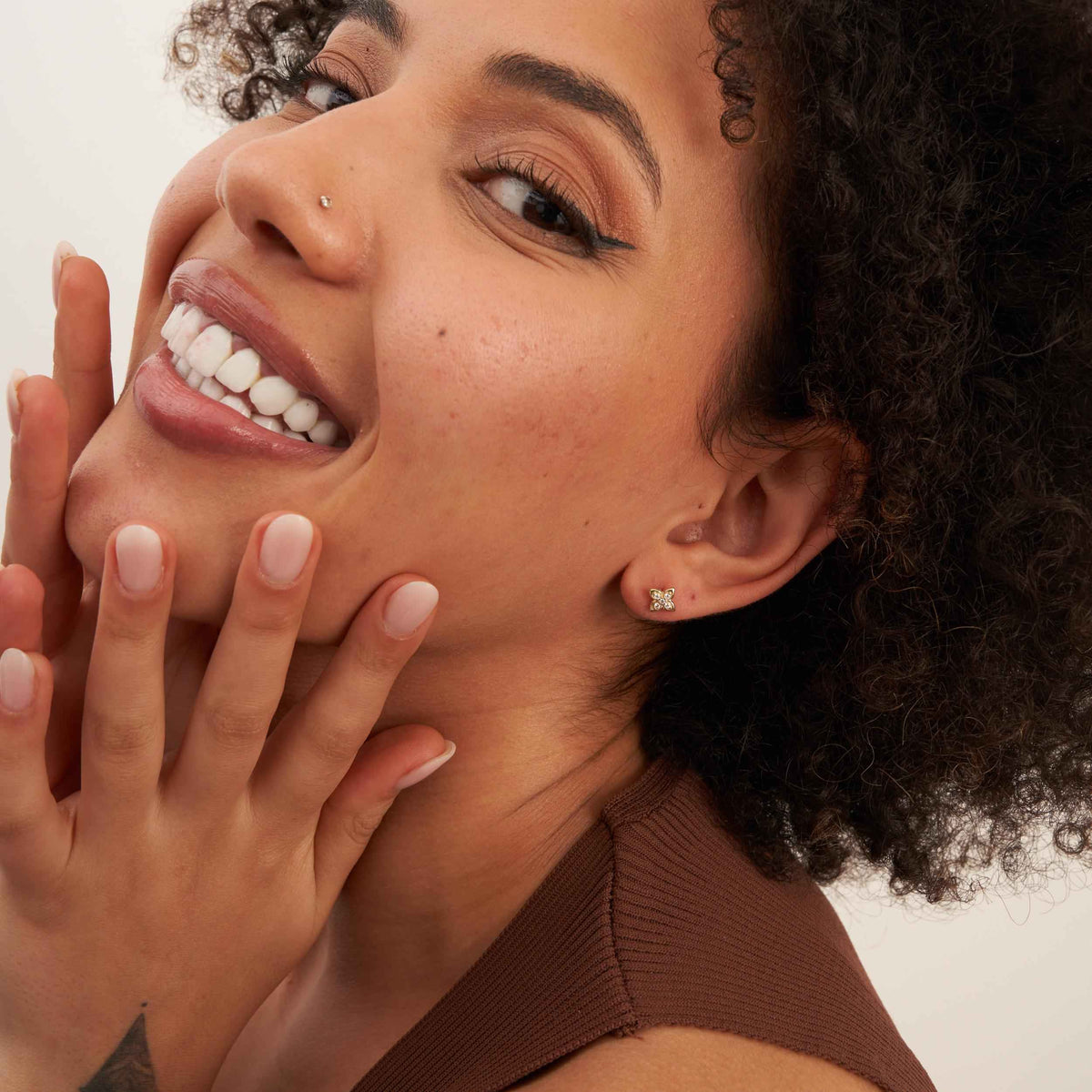 Mannequin souriant, main sur la joue, portant des puces d'oreilles fleur en oxyde de zirconium et or jaune 14 carats