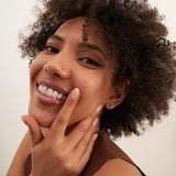 Gros plan sur un mannequin souriant, la main au menton, portant des puces d'oreilles fleur en oxydes de zirconium et or jaune 14 carats