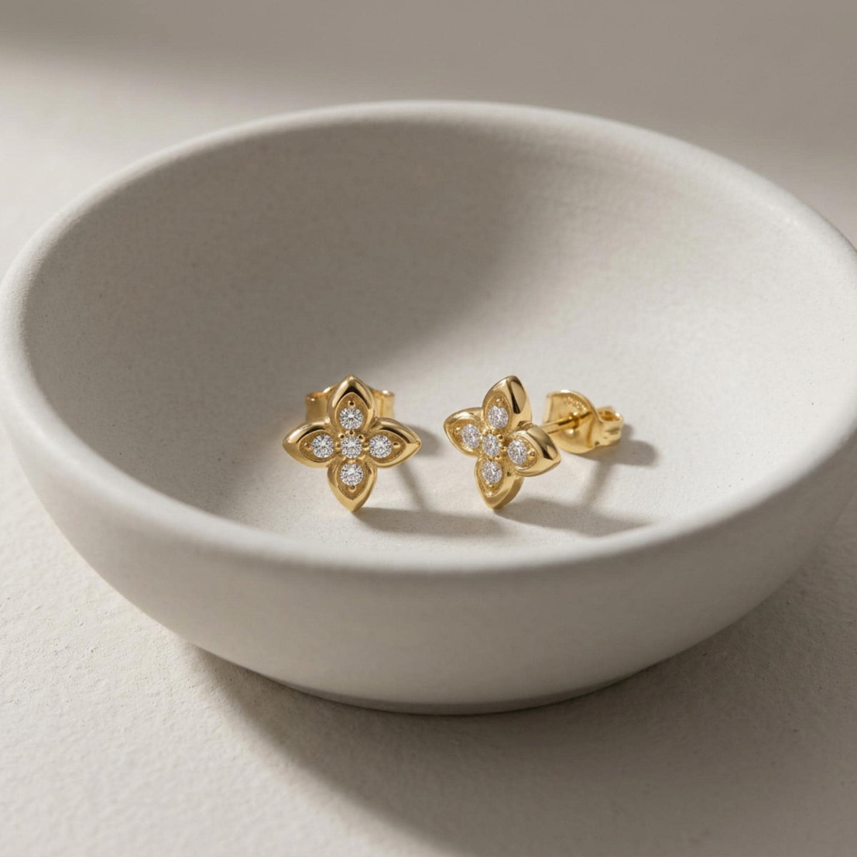 Paire de puces d'oreilles fleur en oxyde de zirconium et or jaune 14 carats dans un bol en céramique