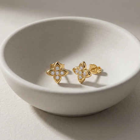 Paire de puces d'oreilles fleur en oxyde de zirconium et or jaune 14 carats dans un bol en céramique