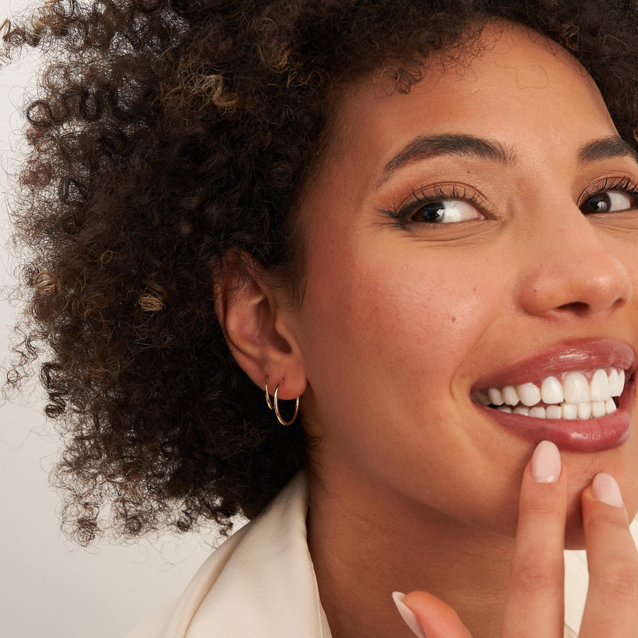 Modella sorridente con un dito sul labbro che indossa orecchini a cerchio endless in oro giallo 14kt