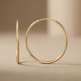 Orecchini a cerchio endless in oro giallo 14kt posati in verticale su una superficie beige
