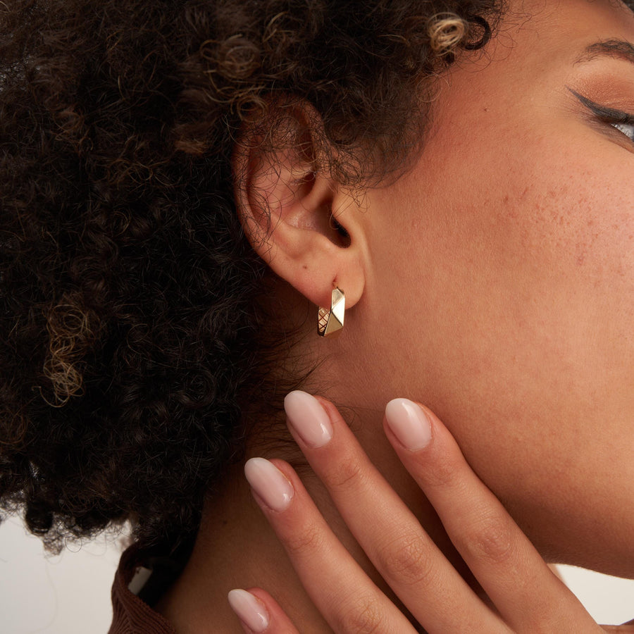 Gros plan de profil sur une créole hexagonale facettée en or jaune 14 carats au lobe