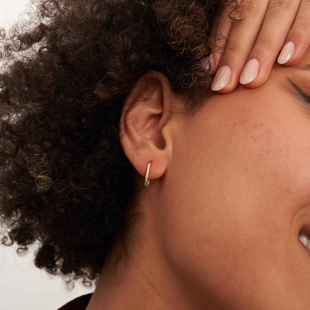 Gros plan d'une oreille, main sur le front, montrant une créole ovale fine en or jaune 14 carats