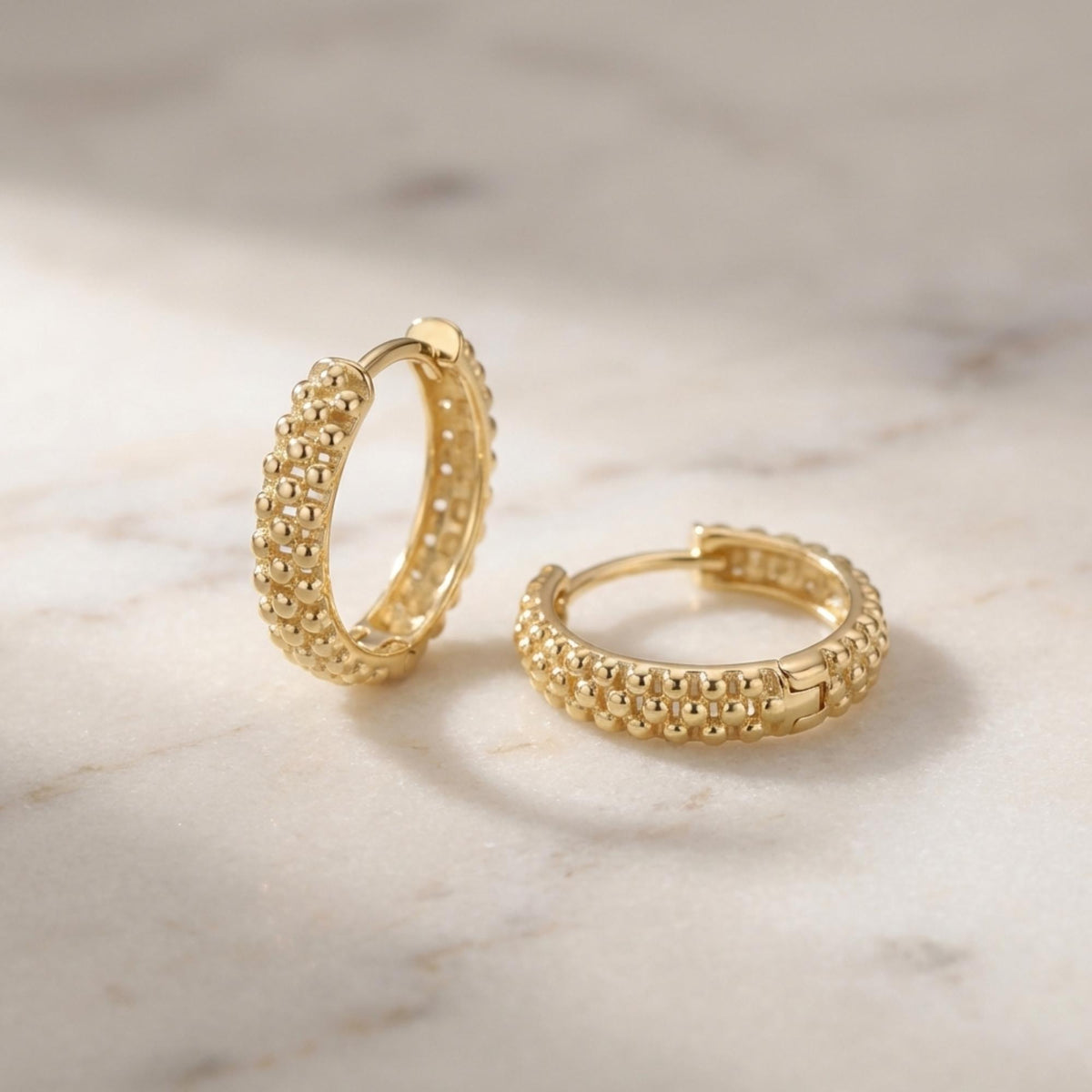 Paire de créoles pointillées en or jaune 14 carats sur du marbre