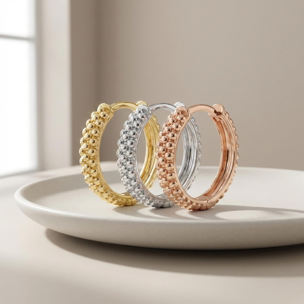 Créoles pointillées en or jaune, blanc et rose 14 carats debout sur une assiette en céramique
