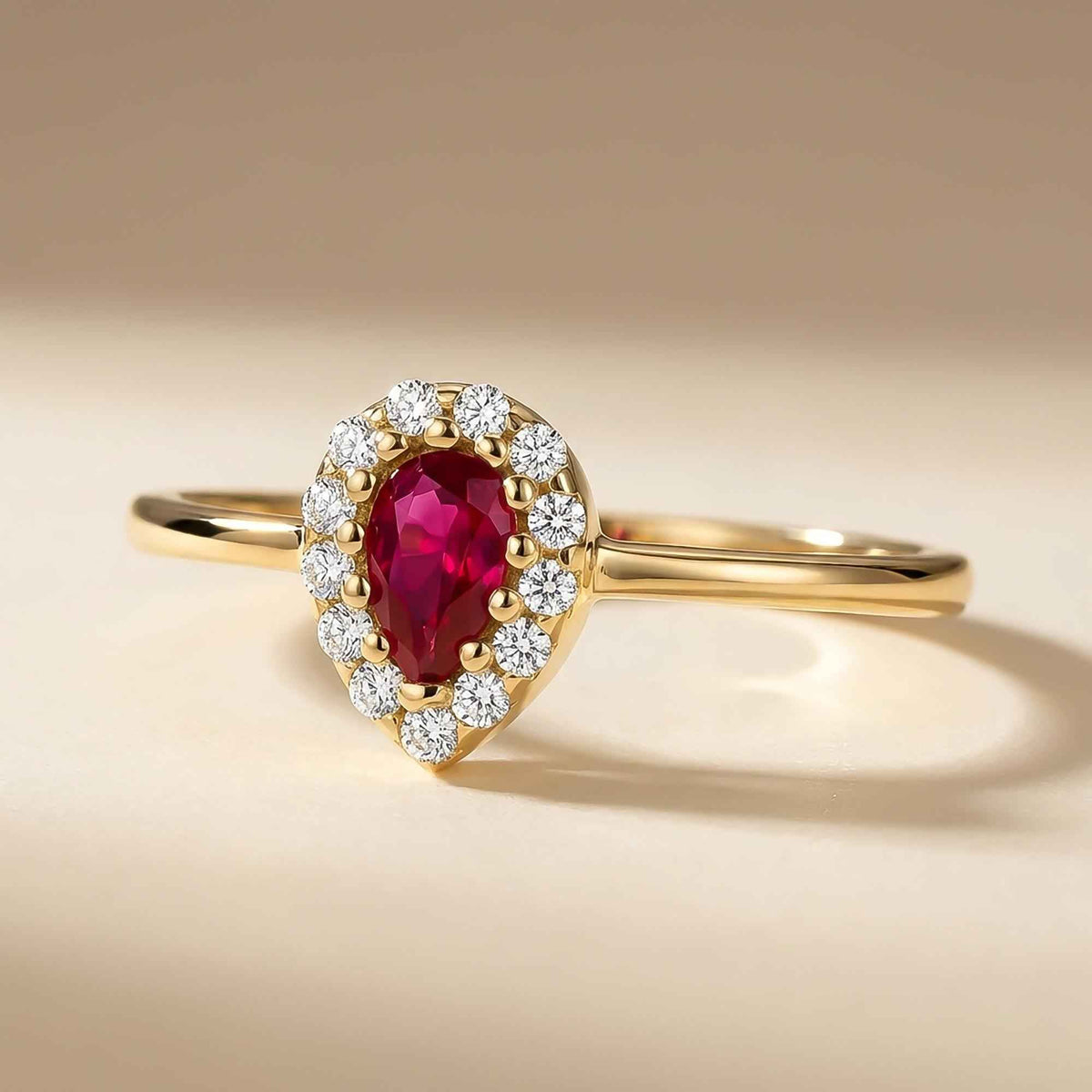 14K yellow gold pear halo ring with lab-grown ruby on beige backdrop