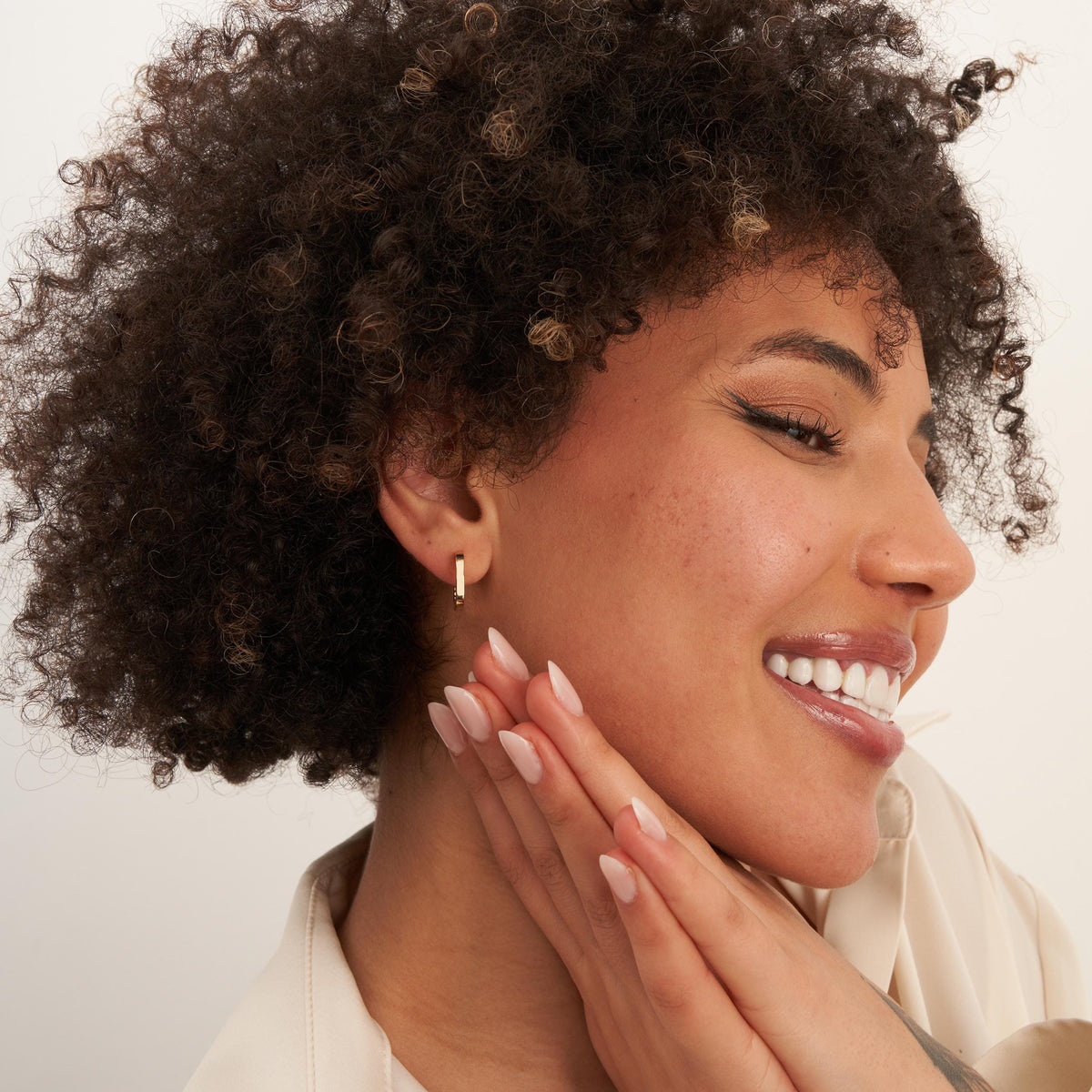 Smiling model with hands at chin wearing 14K yellow gold square hoop earrings