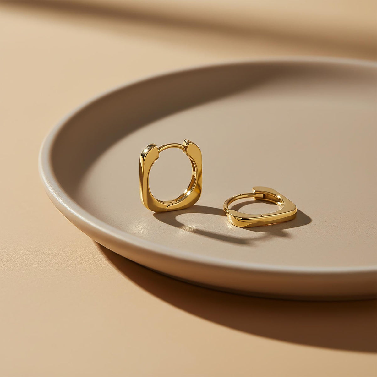 14K yellow gold square hoop earrings on a ceramic dish