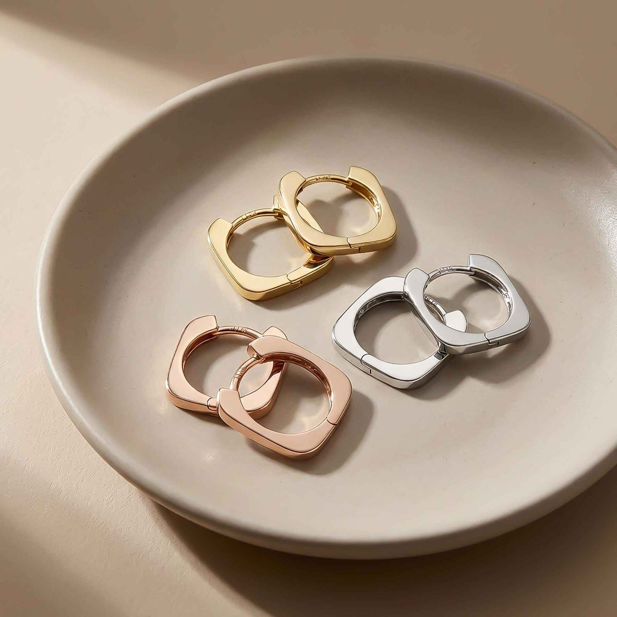 14K yellow, white and rose gold square hoop earrings on a ceramic plate