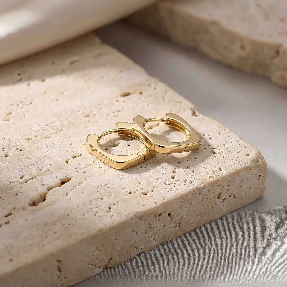 Pair of 14K yellow gold square hoop earrings on travertine stone