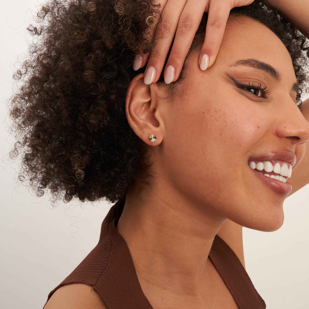 Lächelndes Model mit Hand auf dem Kopf trägt Sonnenstrahl-Ohrstecker aus 585er Gelbgold