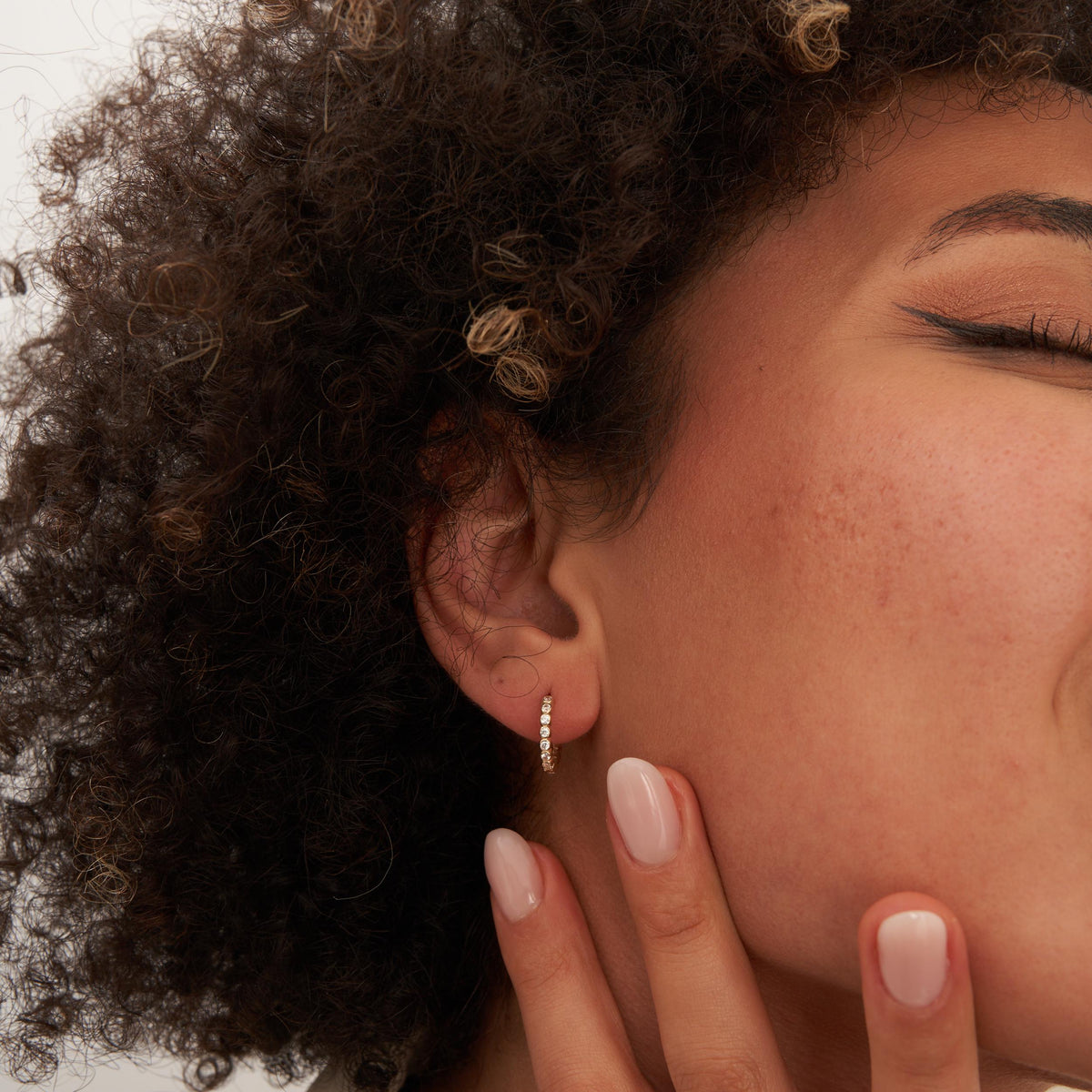 Gros plan sur l'oreille, les yeux fermés et la main à la mâchoire, créole à oxydes de zirconium en serti clos en or jaune 14 carats