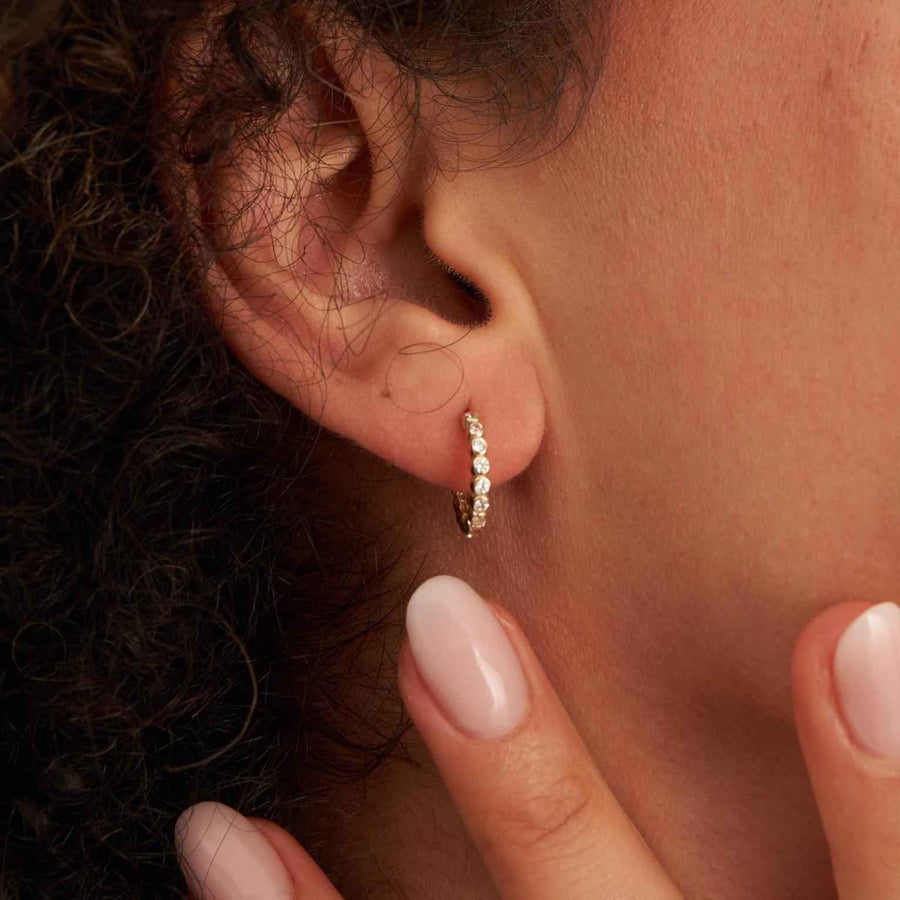 Créole à oxydes de zirconium en serti clos en or jaune 14 carats portée au lobe, gros plan, bout des doigts à la mâchoire