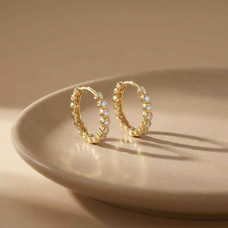 Paire de créoles à oxydes de zirconium en serti clos en or jaune 14 carats debout sur une assiette en céramique