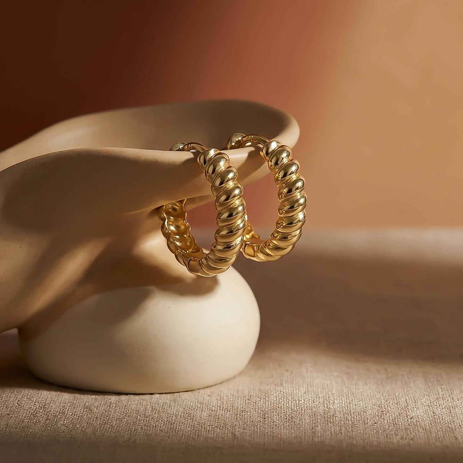 Coppia di orecchini a cerchio ritorti in oro giallo 14kt appoggiati su un supporto in ceramica
