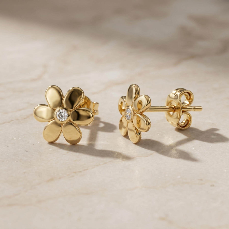 Paire de puces d'oreilles fleur marguerite en or jaune 14 carats sur du travertin, gros plan