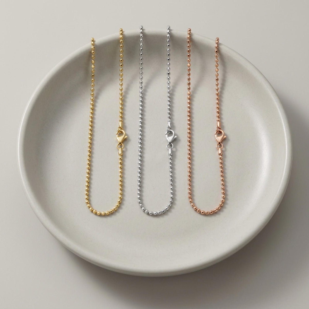 Pulseras de cadena de bolitas en oro amarillo, blanco y rosa de 14 quilates en un plato de cerámica
