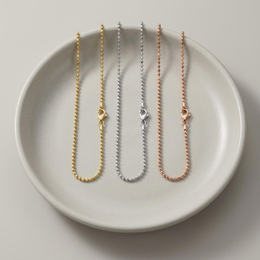 Pulseras de cadena de bolitas en oro amarillo, blanco y rosa de 14 quilates en un plato de cerámica