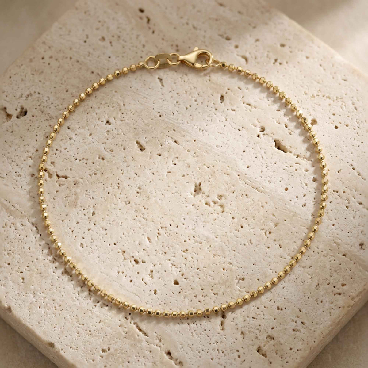 Pulsera de cadena de bolitas en oro amarillo de 14 quilates con cierre de mosquetón sobre piedra de travertino