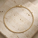 Pulsera de cadena de bolitas en oro amarillo de 14 quilates con cierre de mosquetón sobre piedra de travertino