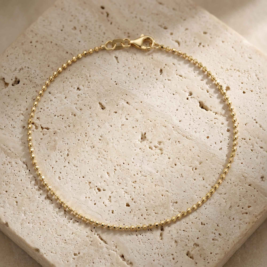 Pulsera de cadena de bolitas en oro amarillo de 14 quilates con cierre de mosquetón sobre piedra de travertino