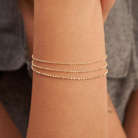 Gros plan sur des bracelets maille boule en or jaune 14 carats superposés au poignet