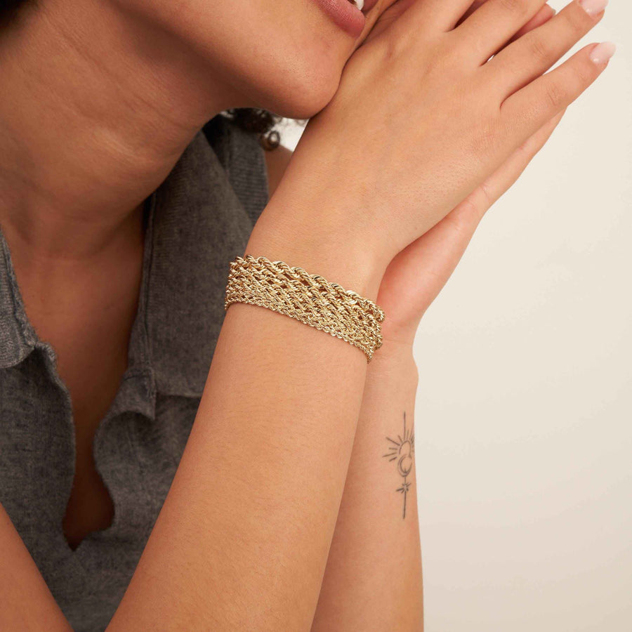 Bracciali a corda in oro giallo 14kt sovrapposti al polso, mani incrociate